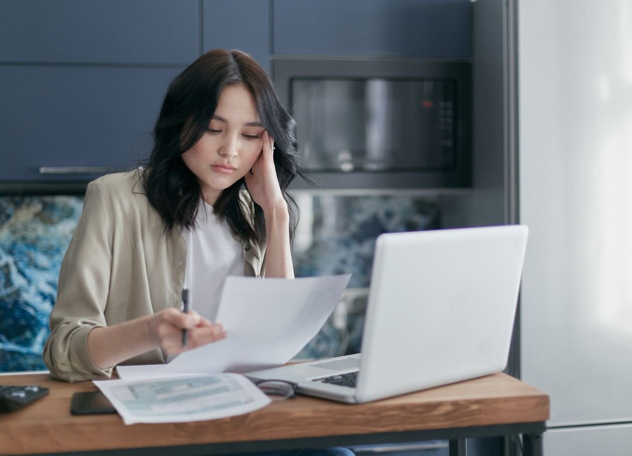 Young woman reviewing savings paperwork and account details on a laptop at home